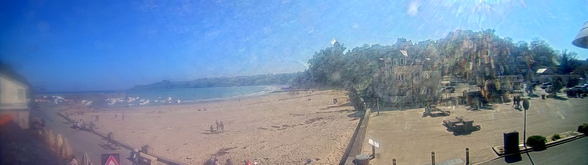A sandy beach with scattered people and boats in the water is overlooked by buildings on a sunny day.