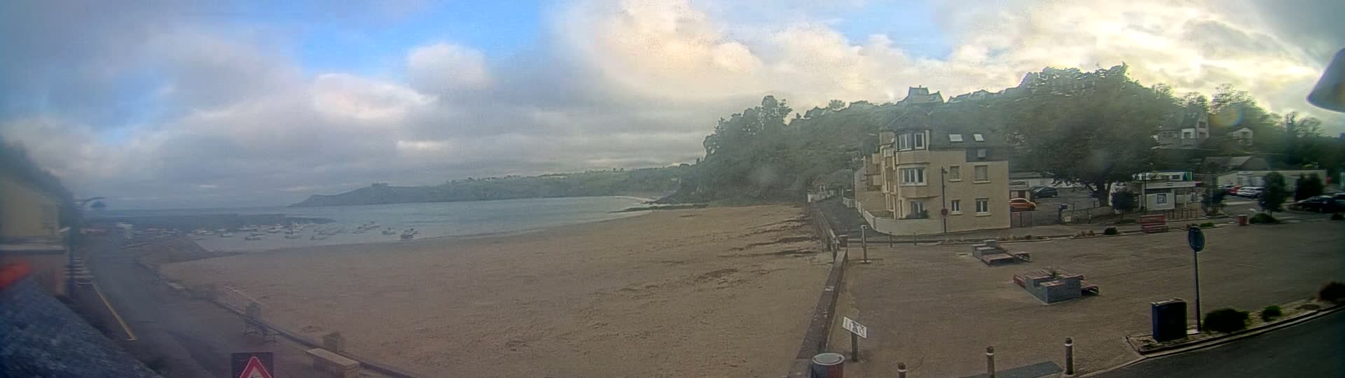 A sandy beach with boats in the water is visible under a partly cloudy sky, with buildings and trees along the shoreline.
