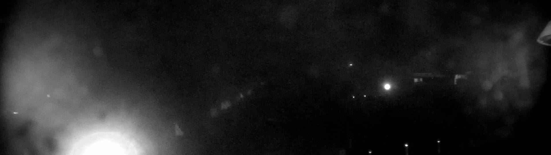A nighttime, hazy, outdoor scene shows indistinct shapes and a few faint lights in the distance.