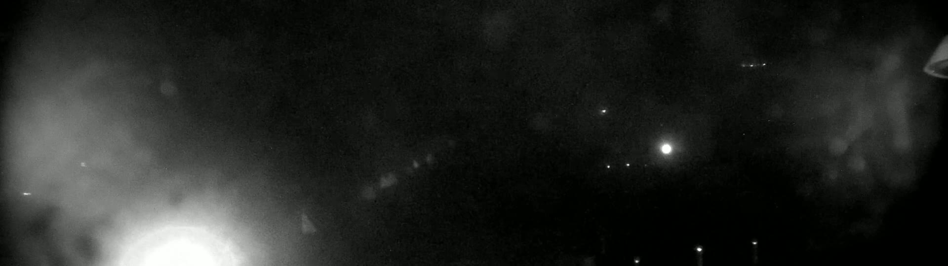 A nighttime, hazy view shows a bright light and several dimmer lights in the distance.
