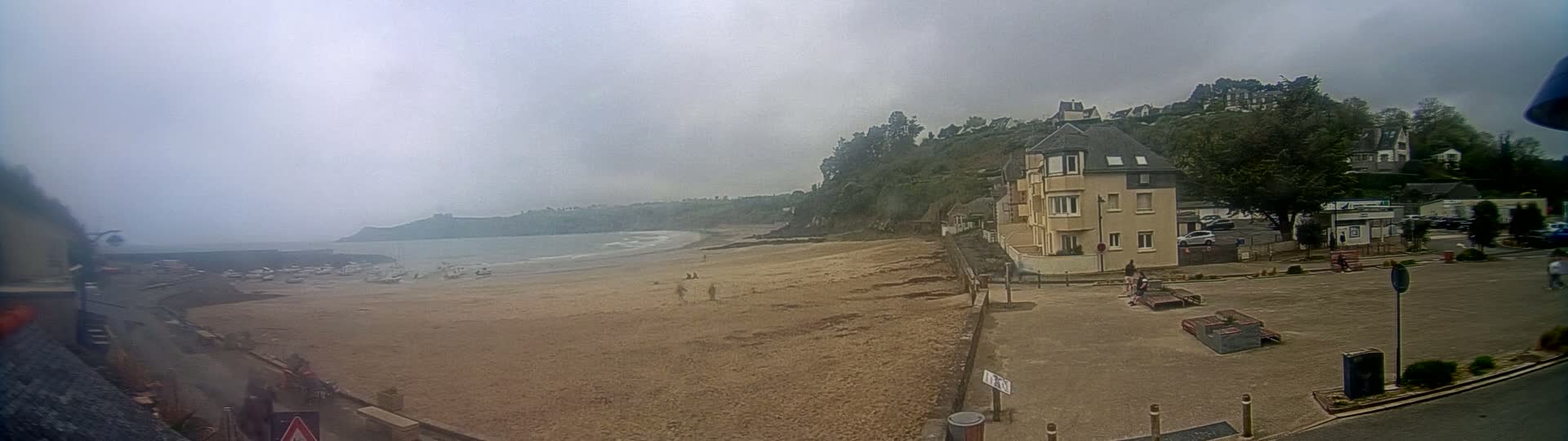 A sandy beach with a few people and boats is visible below a residential area on an overcast day.