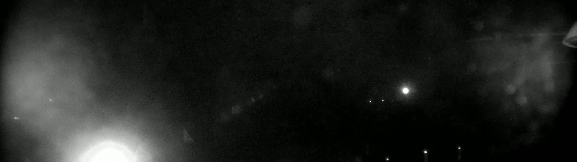 A nighttime, blurry view shows a dark scene with faint lights in the distance and a bright light source near the bottom left.