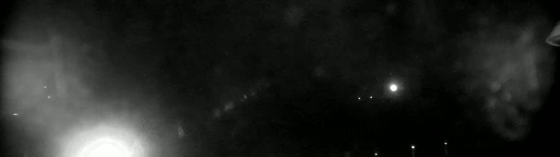 A nighttime outdoor scene shows a bright light in the distance, possibly the moon, with several fainter lights and hazy clouds or fog.