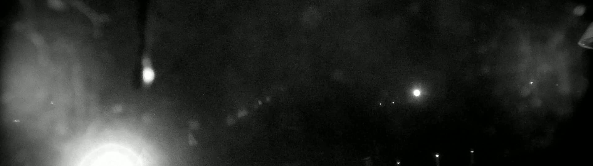 A nighttime scene shows blurry lights in the distance, rain or snow falling in the foreground, and a dark, overcast sky.