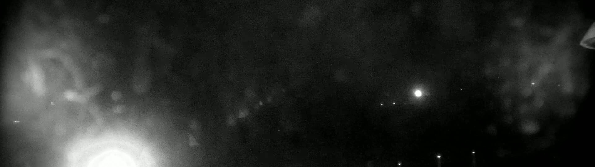 A blurry, nighttime image shows indistinct shapes and bright lights against a dark, possibly foggy or hazy, sky.