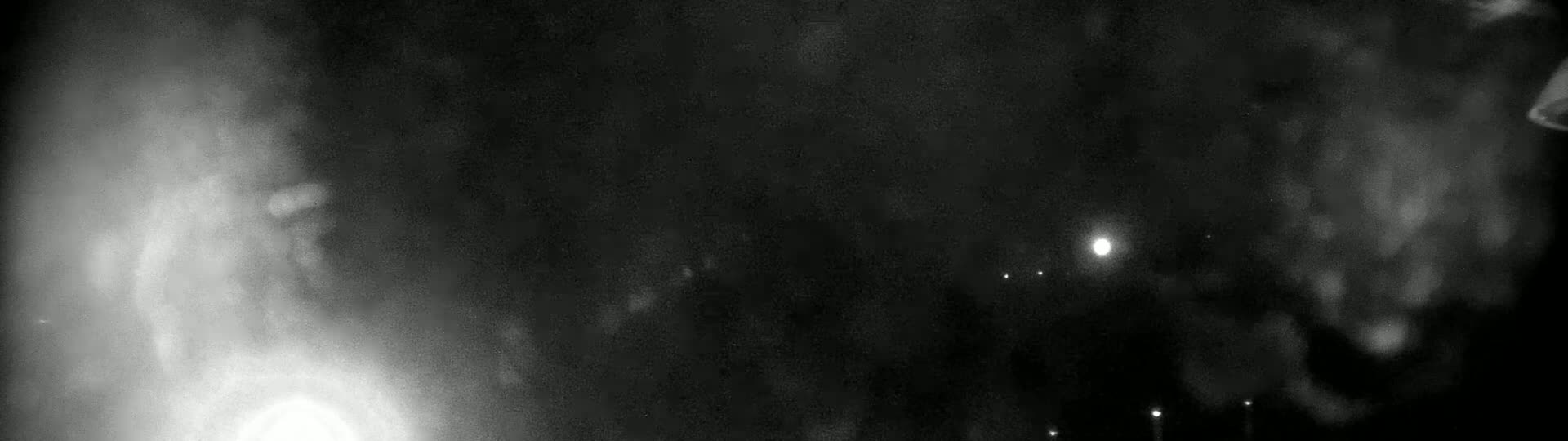 A nighttime, blurry image shows bright lights and hazy clouds or fog in the distance.