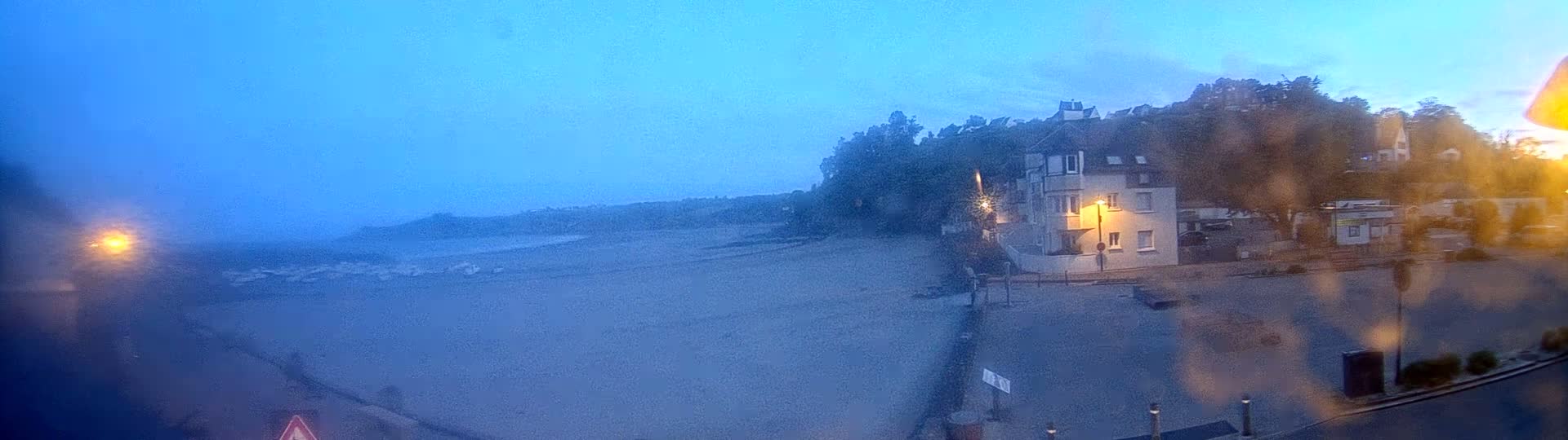A hazy, dusky view shows a mostly empty beach, a building, and a parking lot, all seen through a rain-streaked window.