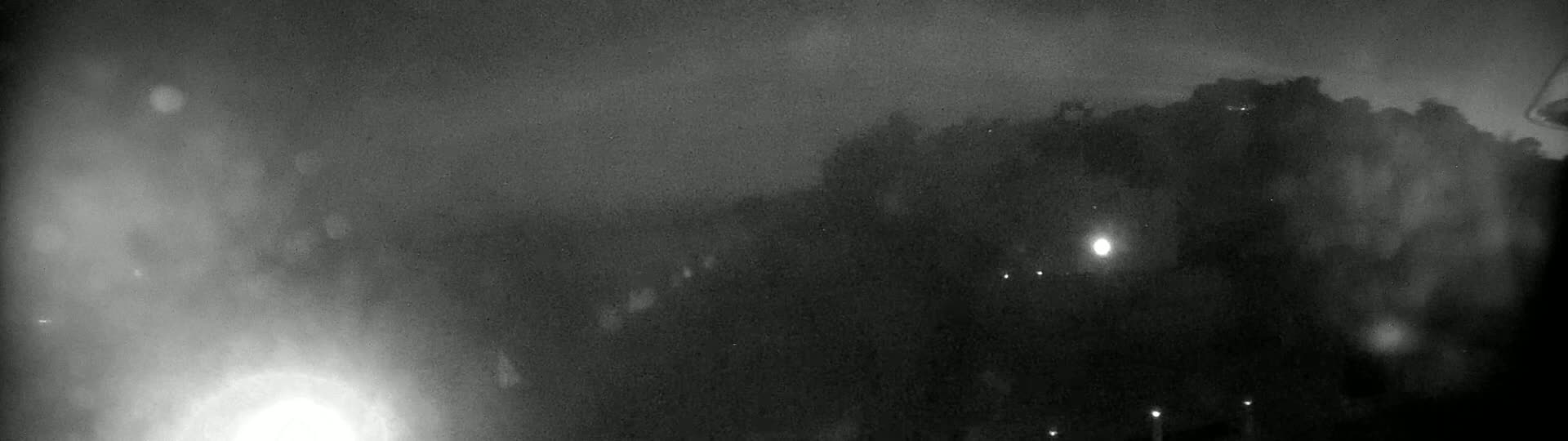 A hazy, dark night scene shows a silhouetted hilltop with a few small lights visible in the distance.