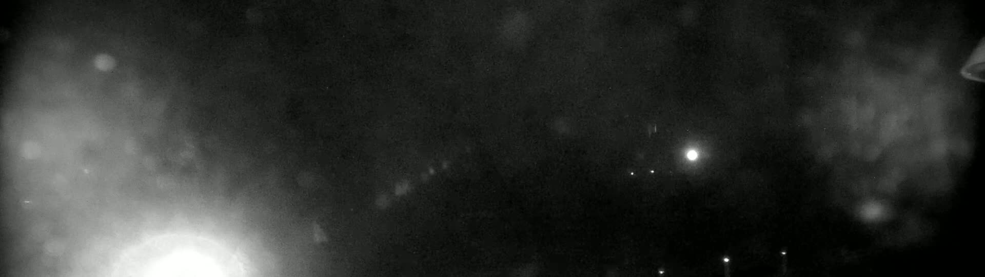 A dark, nighttime scene with hazy, snowy conditions shows a few distant lights and a bright light source in the bottom left corner.