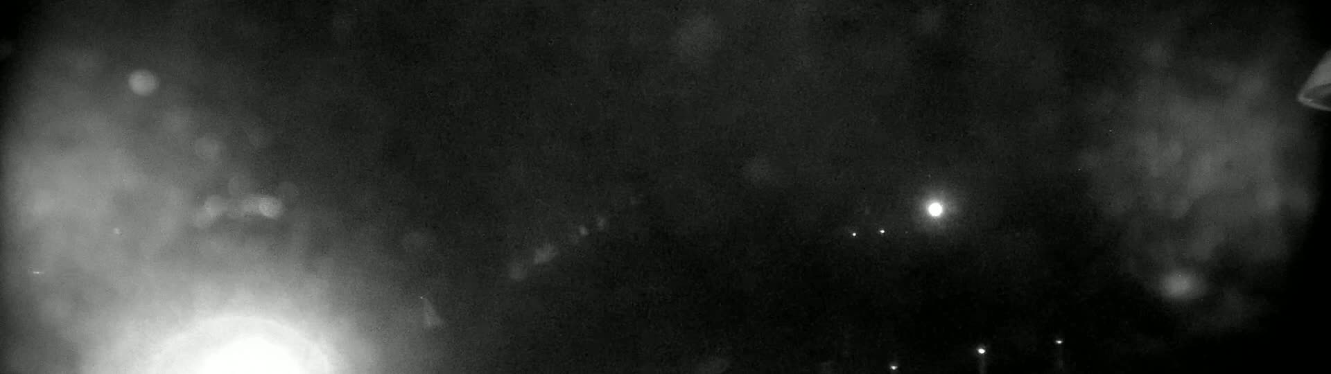 A nighttime outdoor scene shows hazy light sources in the distance and brighter lights closer to the camera, possibly from vehicles.