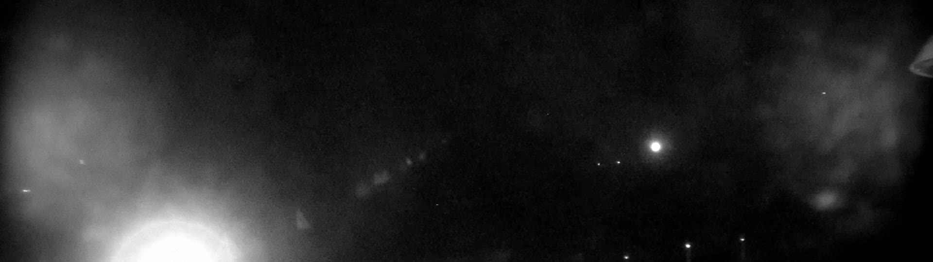 A nighttime outdoor scene shows a bright light source in the bottom left corner and several fainter lights scattered across a dark, hazy sky.