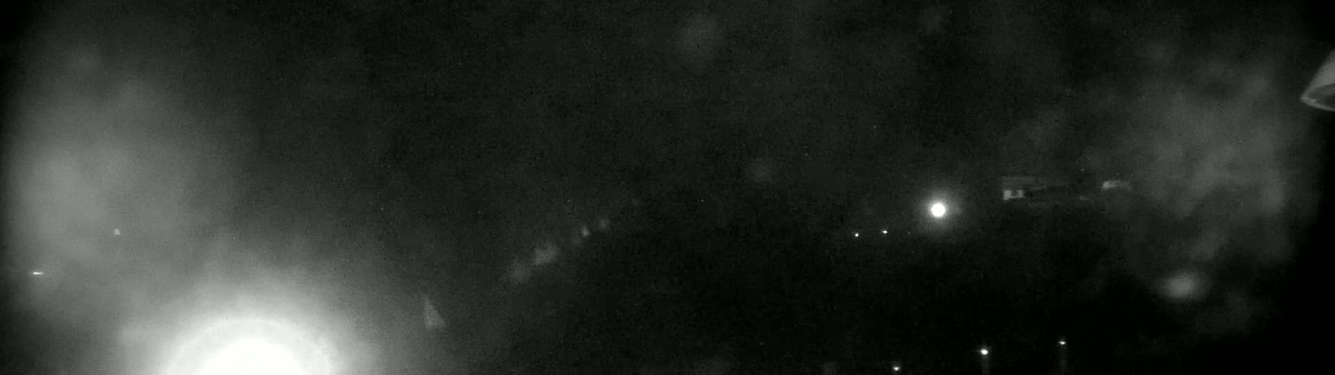 A nighttime, hazy, outdoor scene shows a few distant lights, possibly from buildings or vehicles, with a bright light source near the bottom left corner.