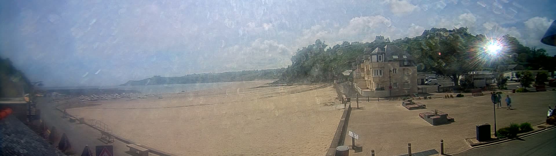 A sandy beach stretches alongside a seaside town under a partly sunny sky, with a building prominently situated near the beach's edge.