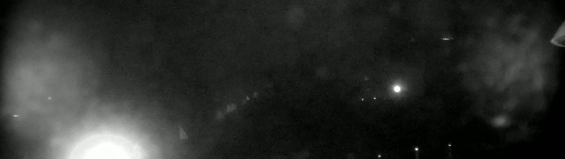 A nighttime, hazy or foggy scene shows a few distant lights and a bright light possibly a light source or the moon.