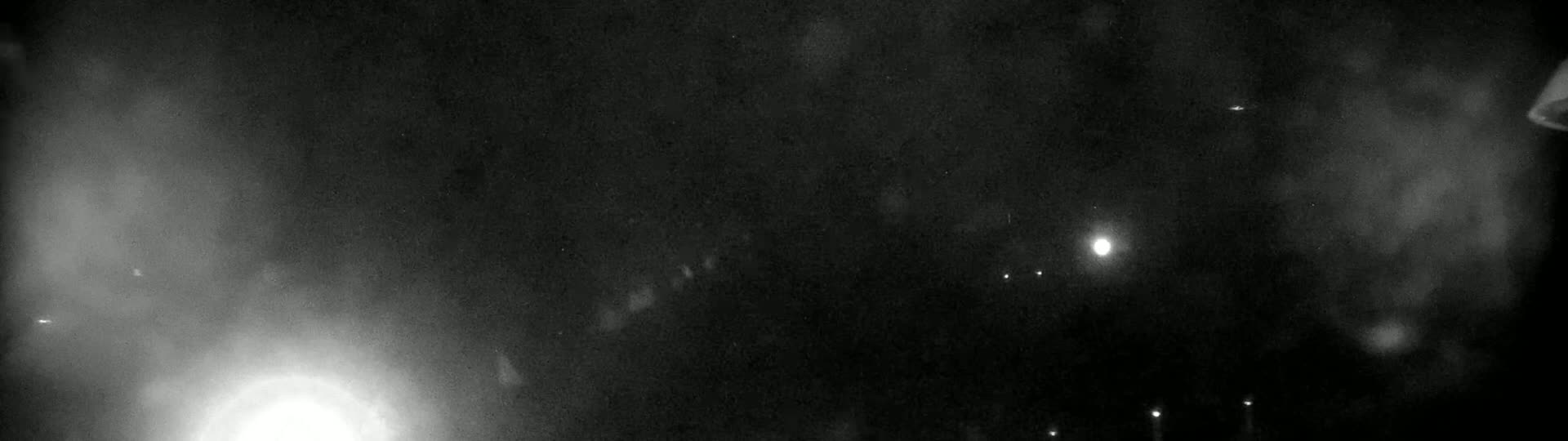 A nighttime view shows a hazy, dark sky with several bright lights and a brighter light in the lower-left.