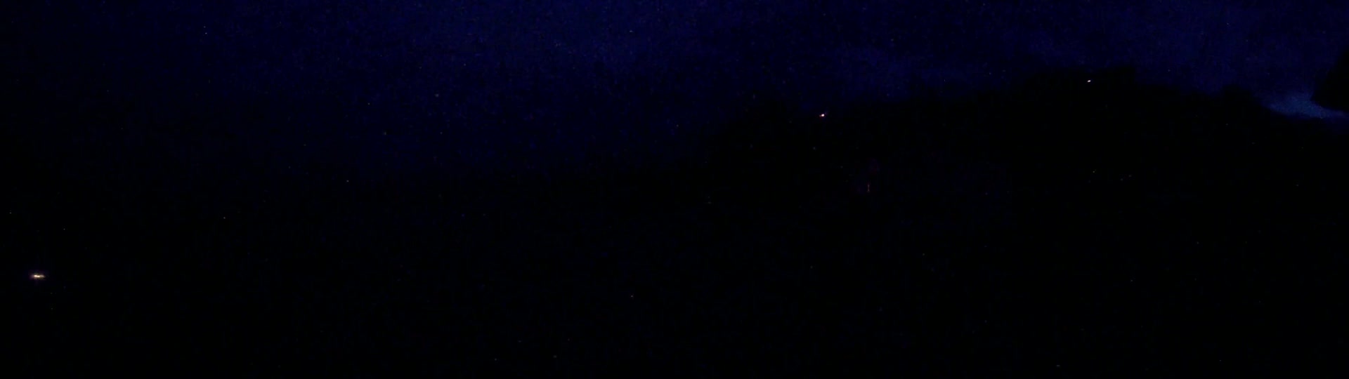 A nighttime, dark sky speckled with stars and a distant, dark landmass is visible under a cloudy, possibly rainy sky.