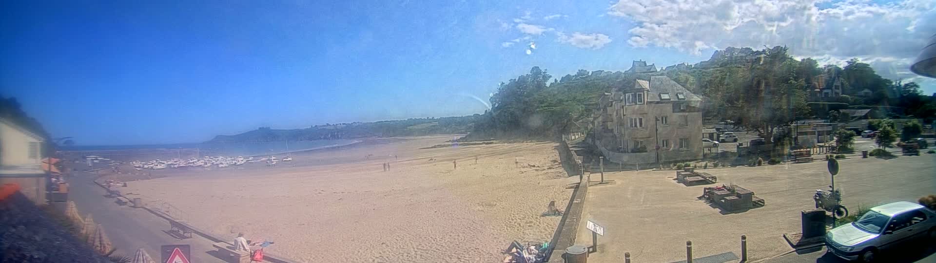A sandy beach with boats on the water is visible from a seaside town on a sunny day with a few clouds.