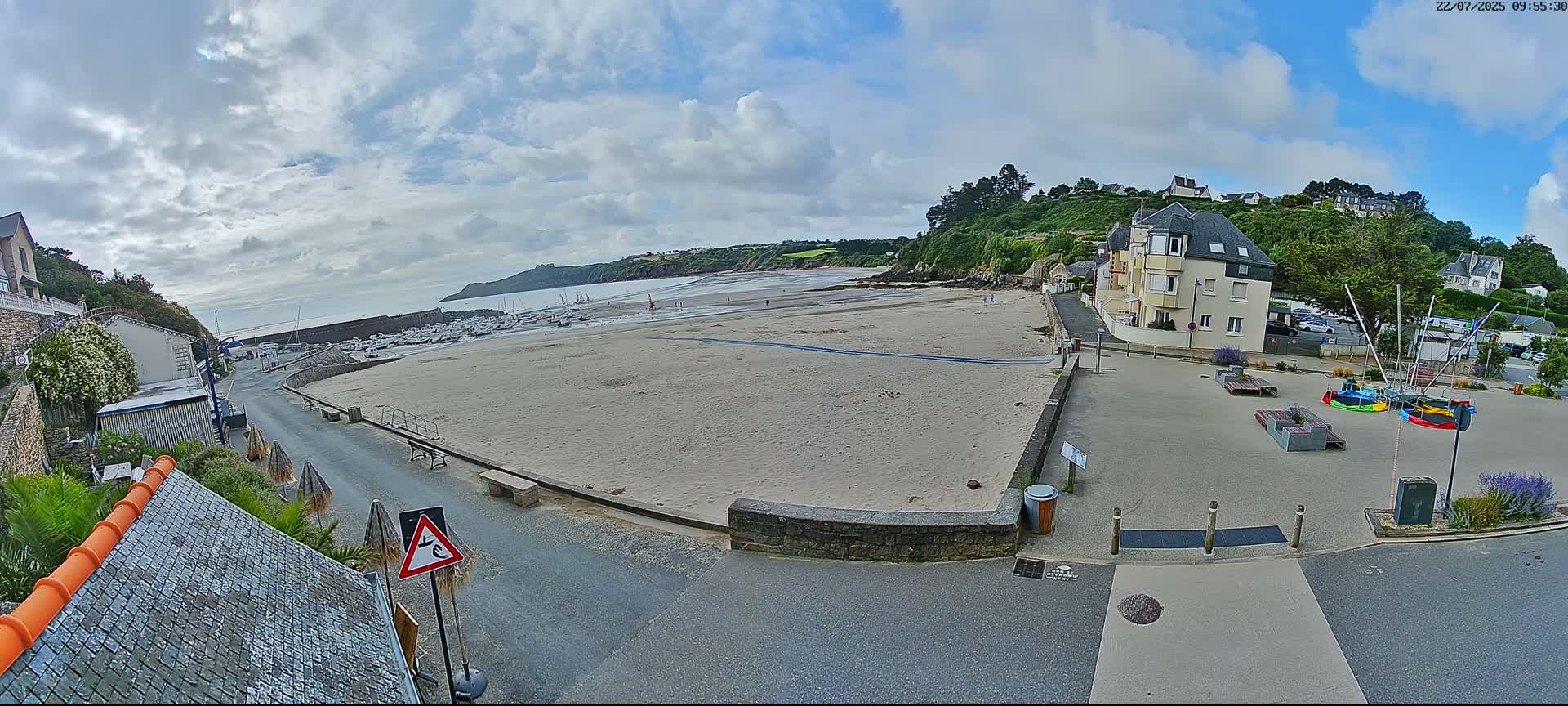 A mostly sunny day reveals a sandy beach with boats at low tide, a small town with buildings and a paved area with playground equipment.