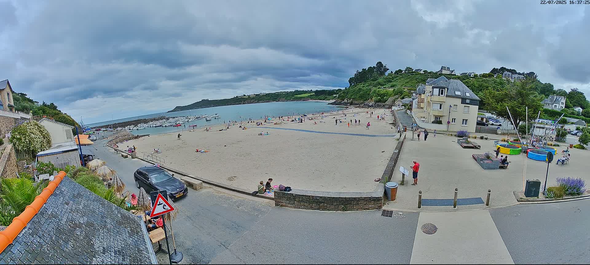 A mostly sunny day reveals a sandy beach with boats at low tide, a small town with buildings and a paved area with playground equipment.