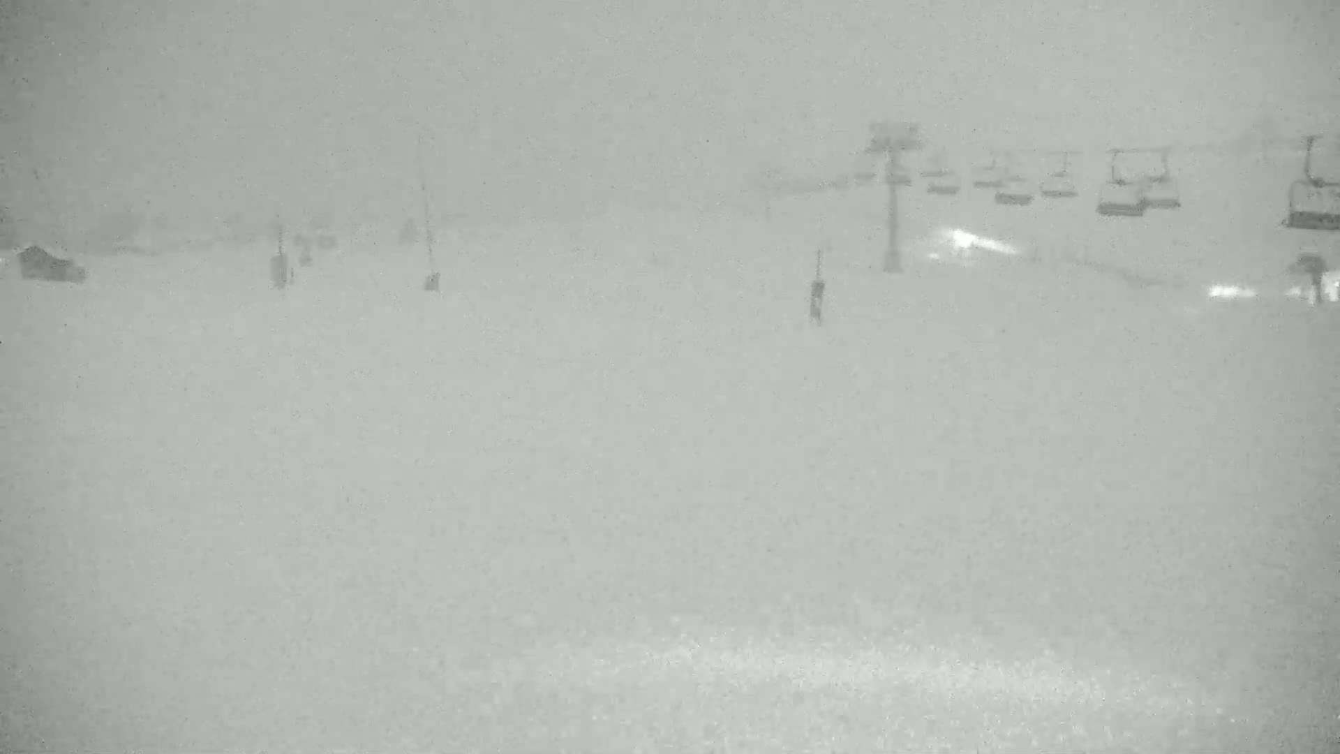 A snow-covered ski slope with a chairlift in the background during a heavy snowstorm.