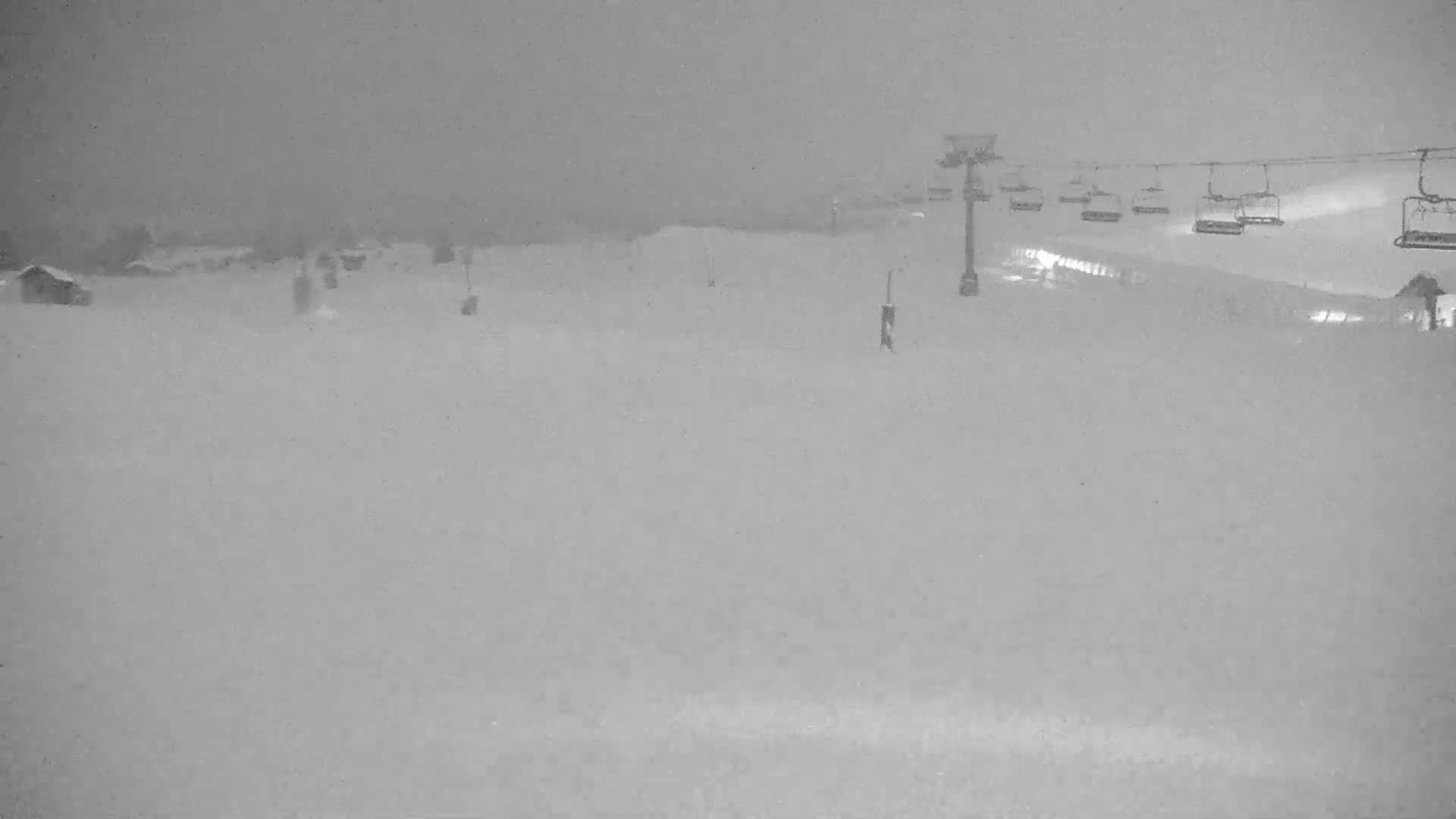 A snow-covered ski slope with a chairlift in the background during a heavy snowstorm.