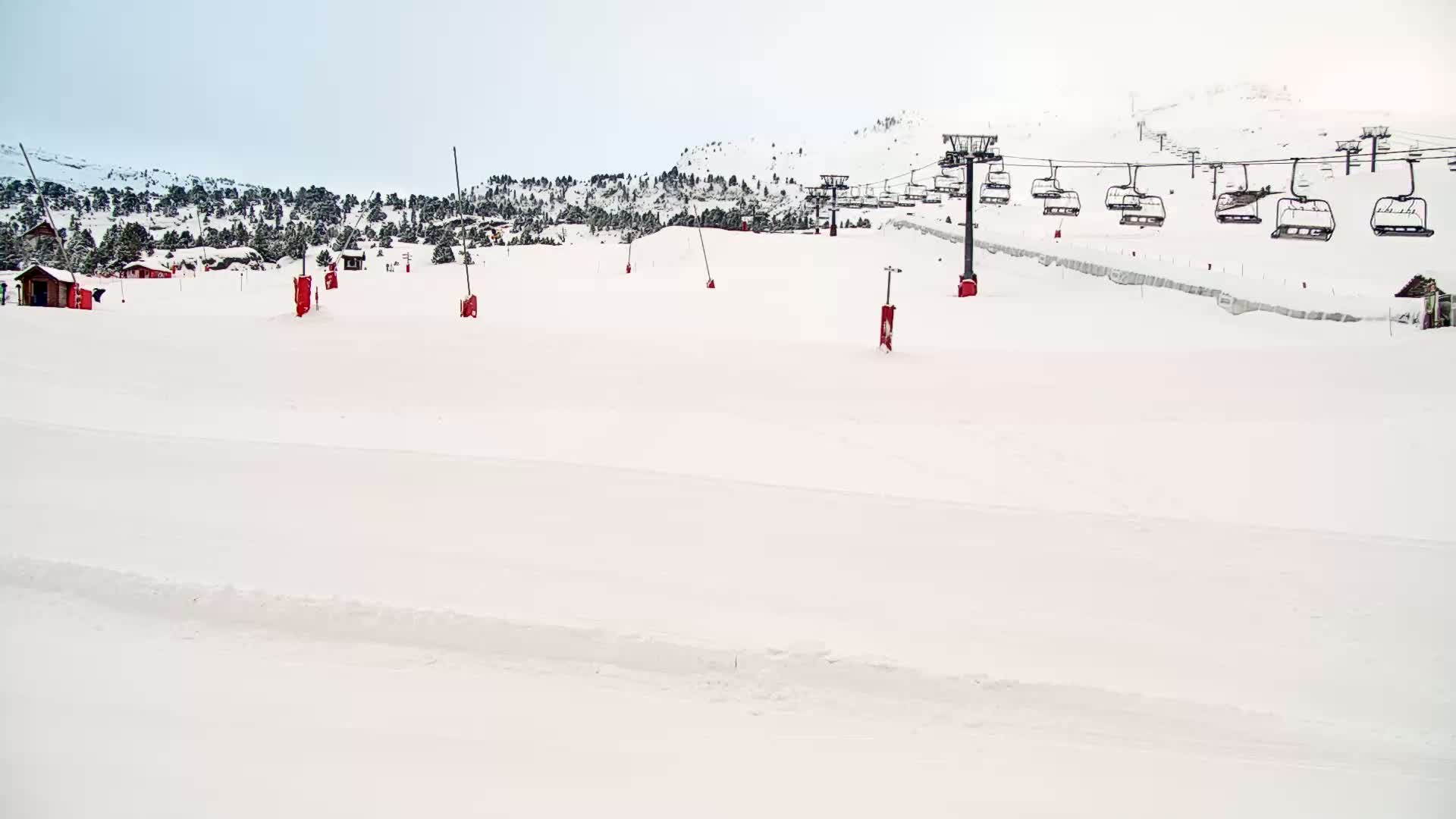 A snow-covered ski slope with a chairlift in the background on an overcast day.