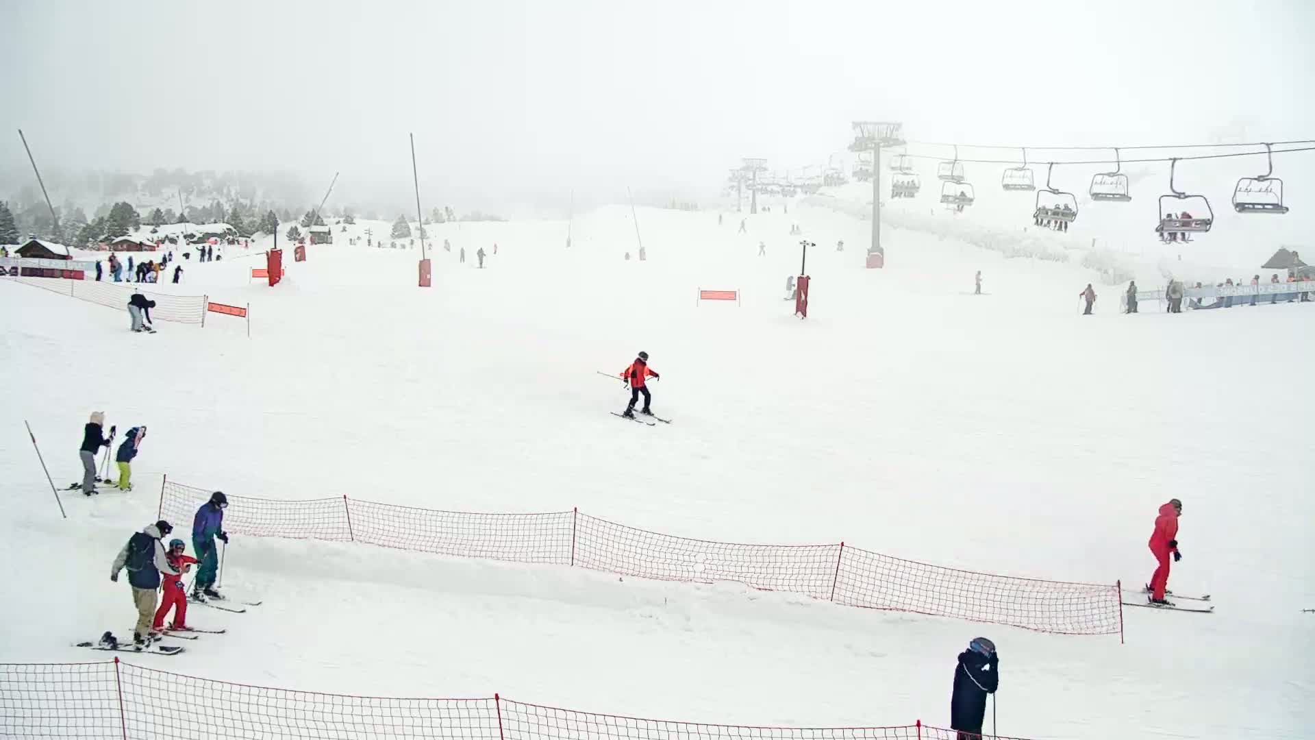 Several skiers and snowboarders are scattered across a snow-covered ski slope on an overcast day, with a chairlift visible in the background.