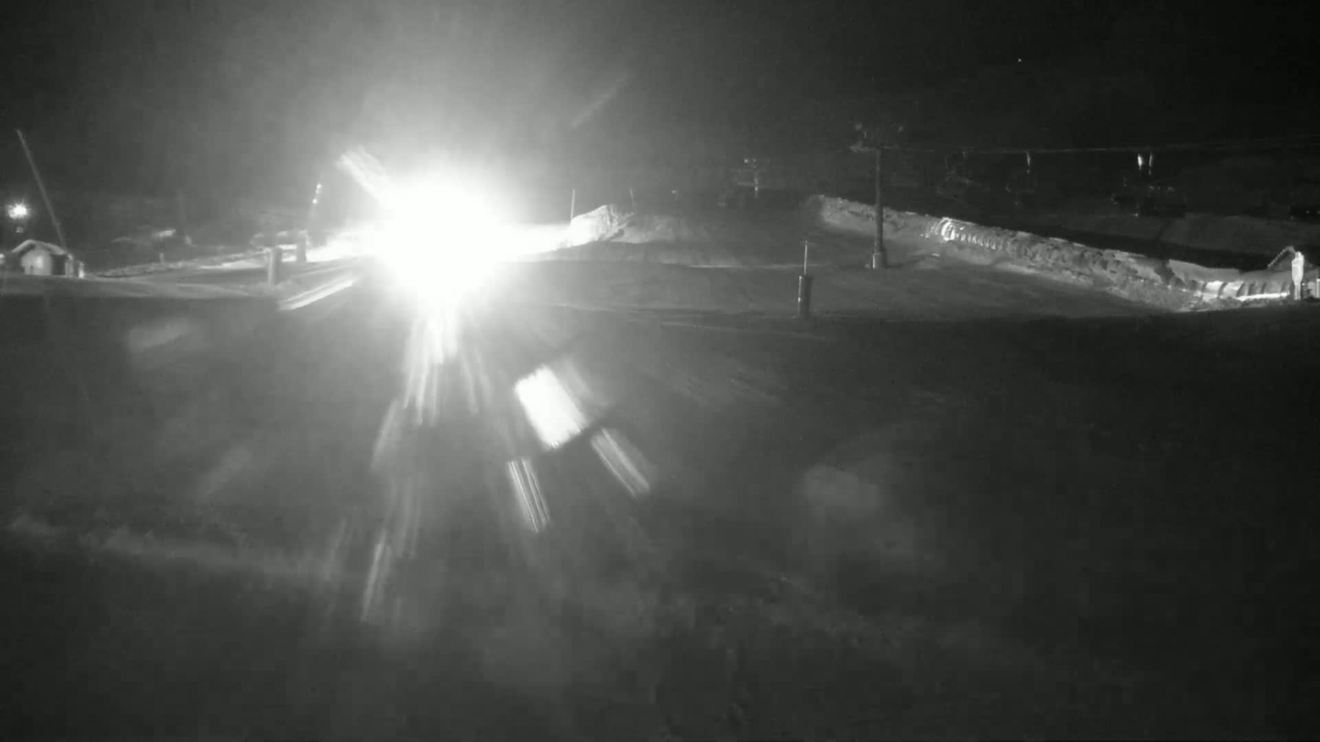 A bright light shines across a snow-covered landscape at night.
