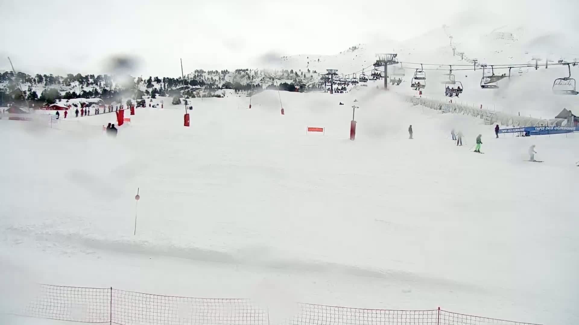 A snowy ski slope with a chairlift and several skiers visible through a rain-covered lens.