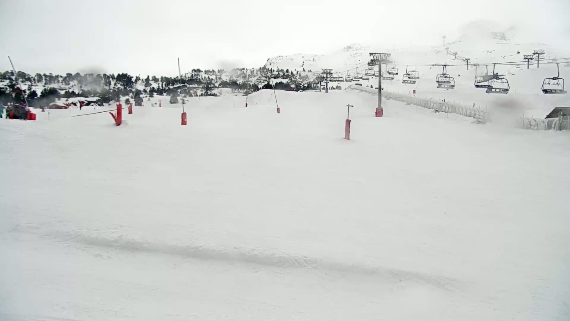 A snow-covered ski slope with a chairlift in the background under overcast skies.