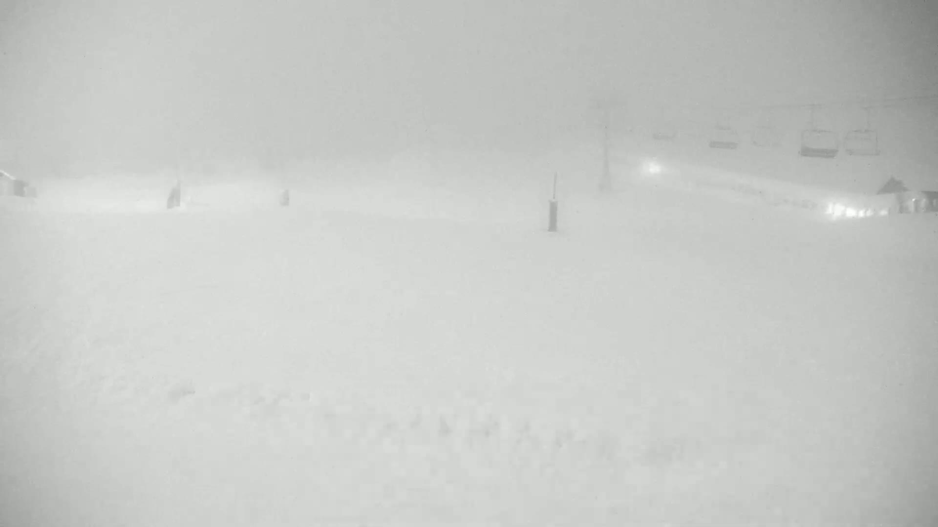 A snow-covered landscape is barely visible through heavy fog or blowing snow, with a chairlift faintly seen in the background.