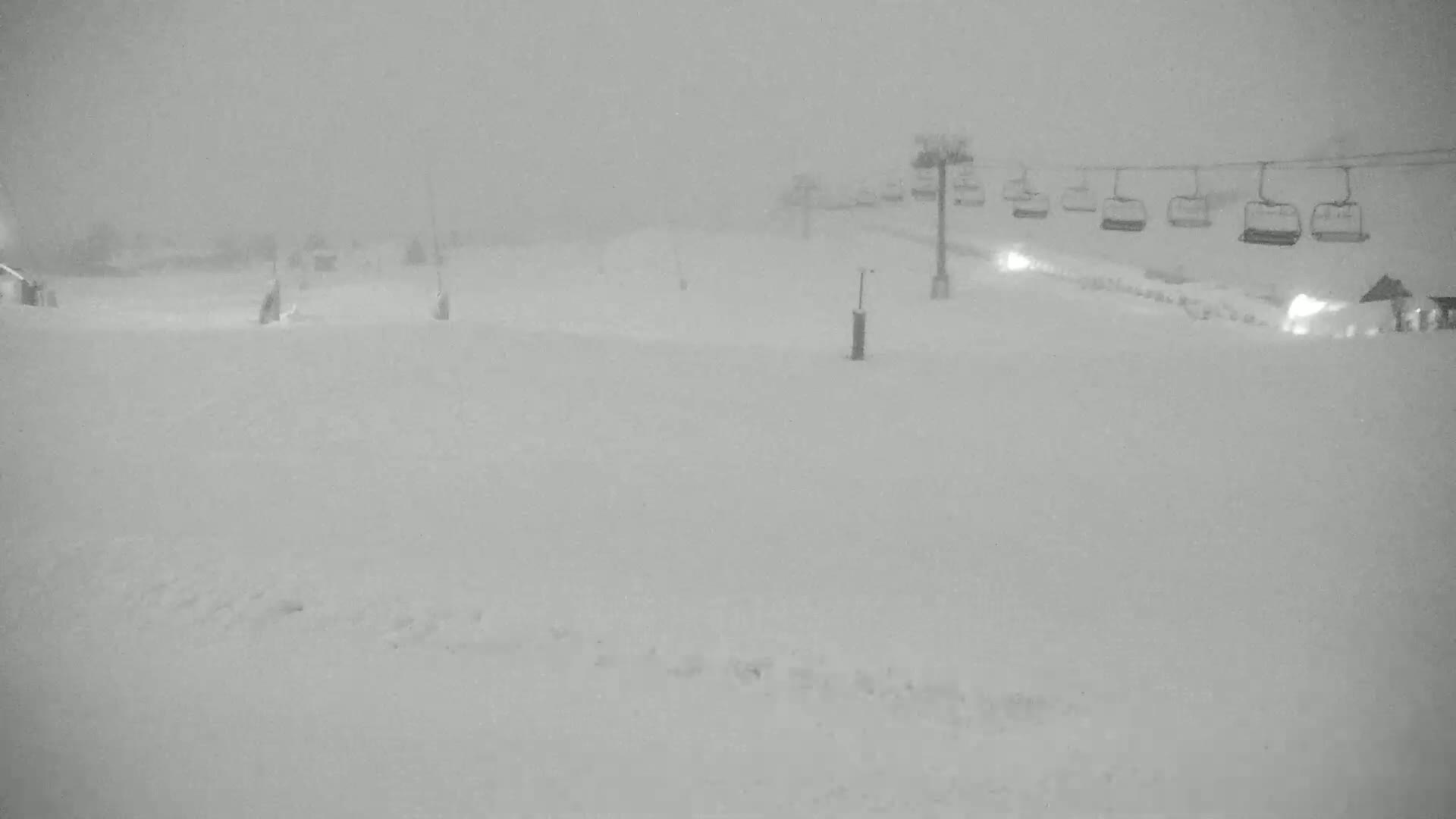 A snow-covered ski slope with a chairlift in the background during a heavy snowstorm.