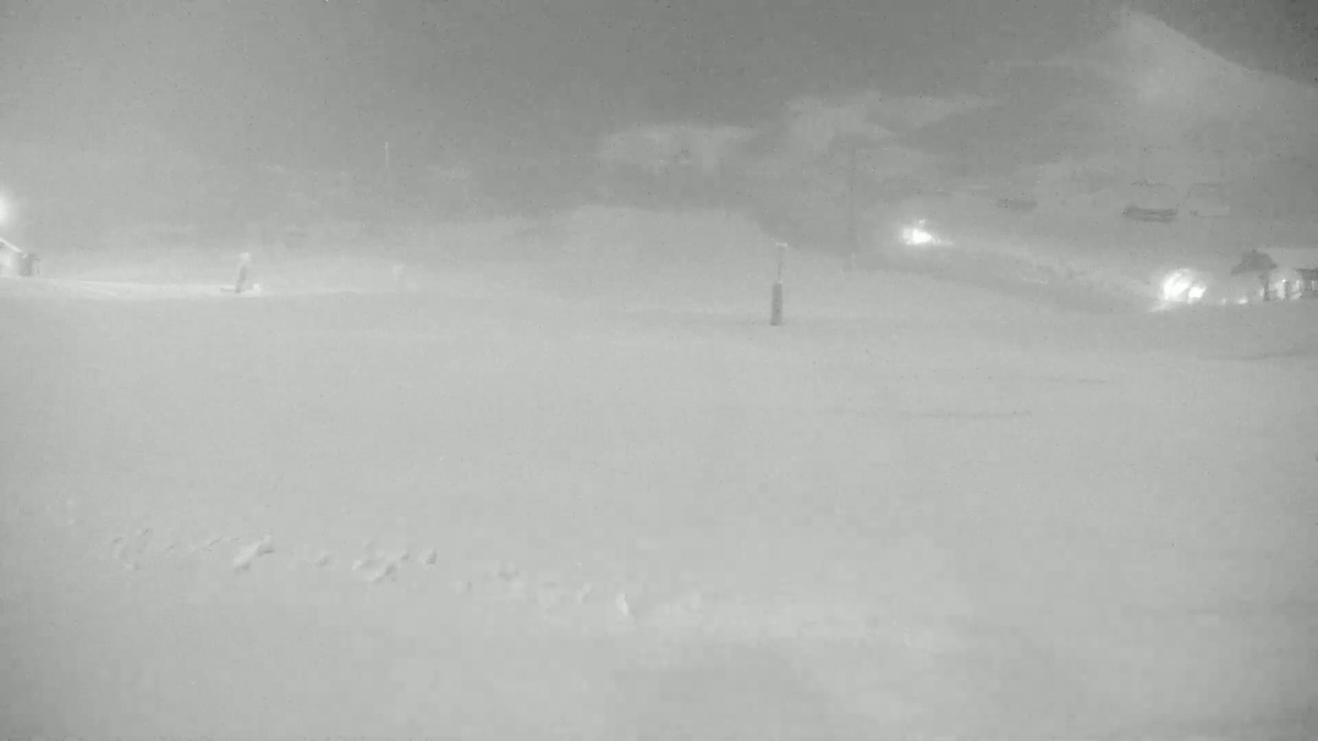 A snow-covered, dimly lit area is seen at night during a snowstorm.