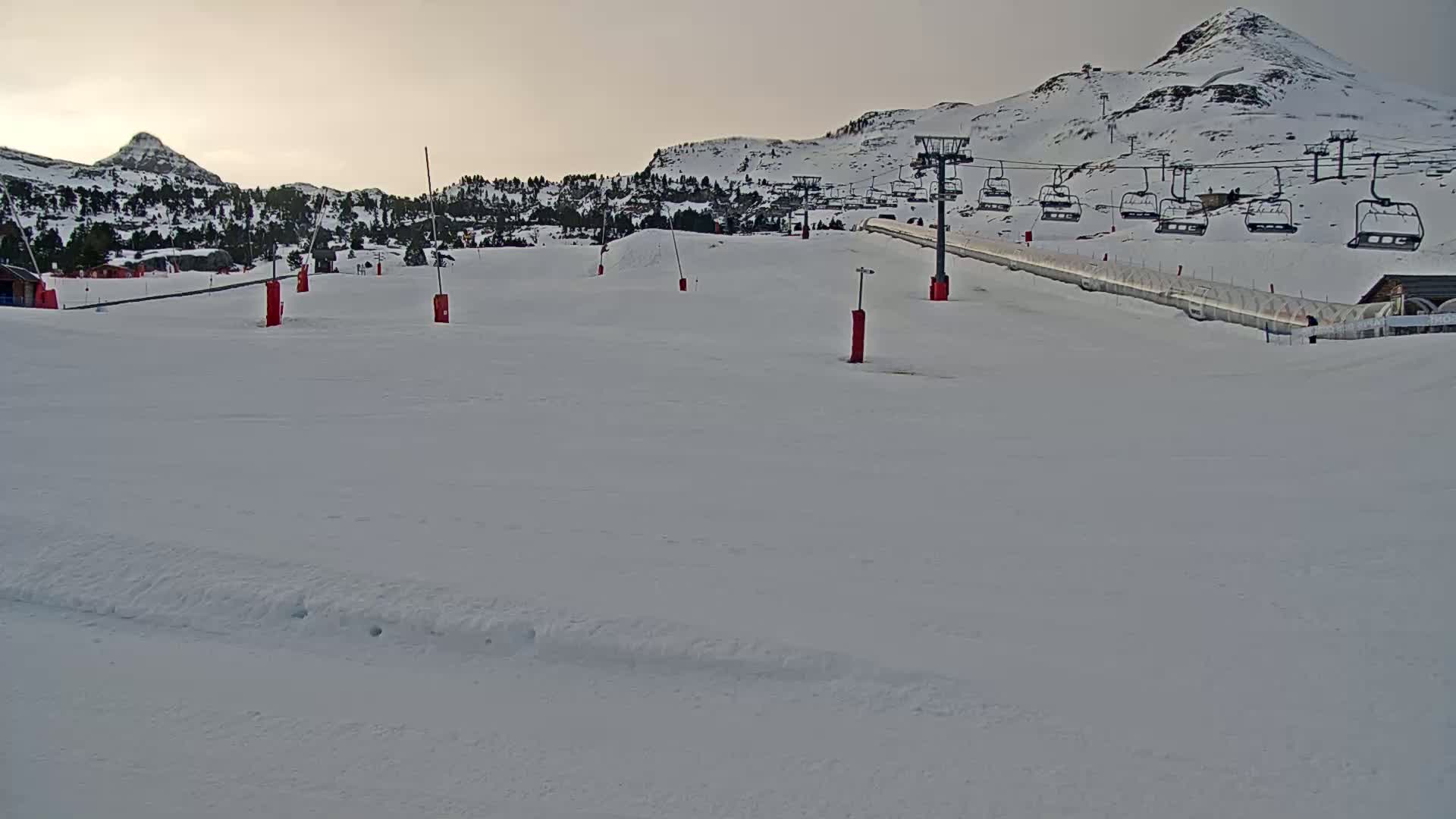A snow-covered ski slope with a chairlift and several markers under a cloudy sky is visible, with mountains in the background.