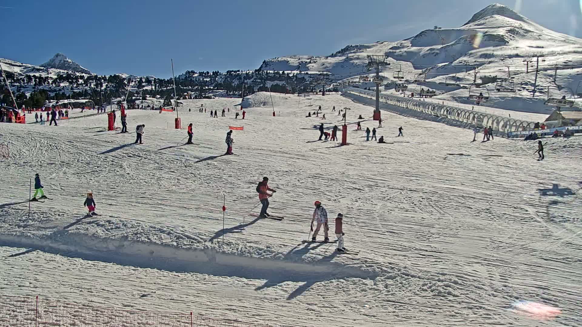 A sunny day on a snow-covered ski slope with numerous skiers and snowboarders of varying skill levels enjoying the mountain scenery.