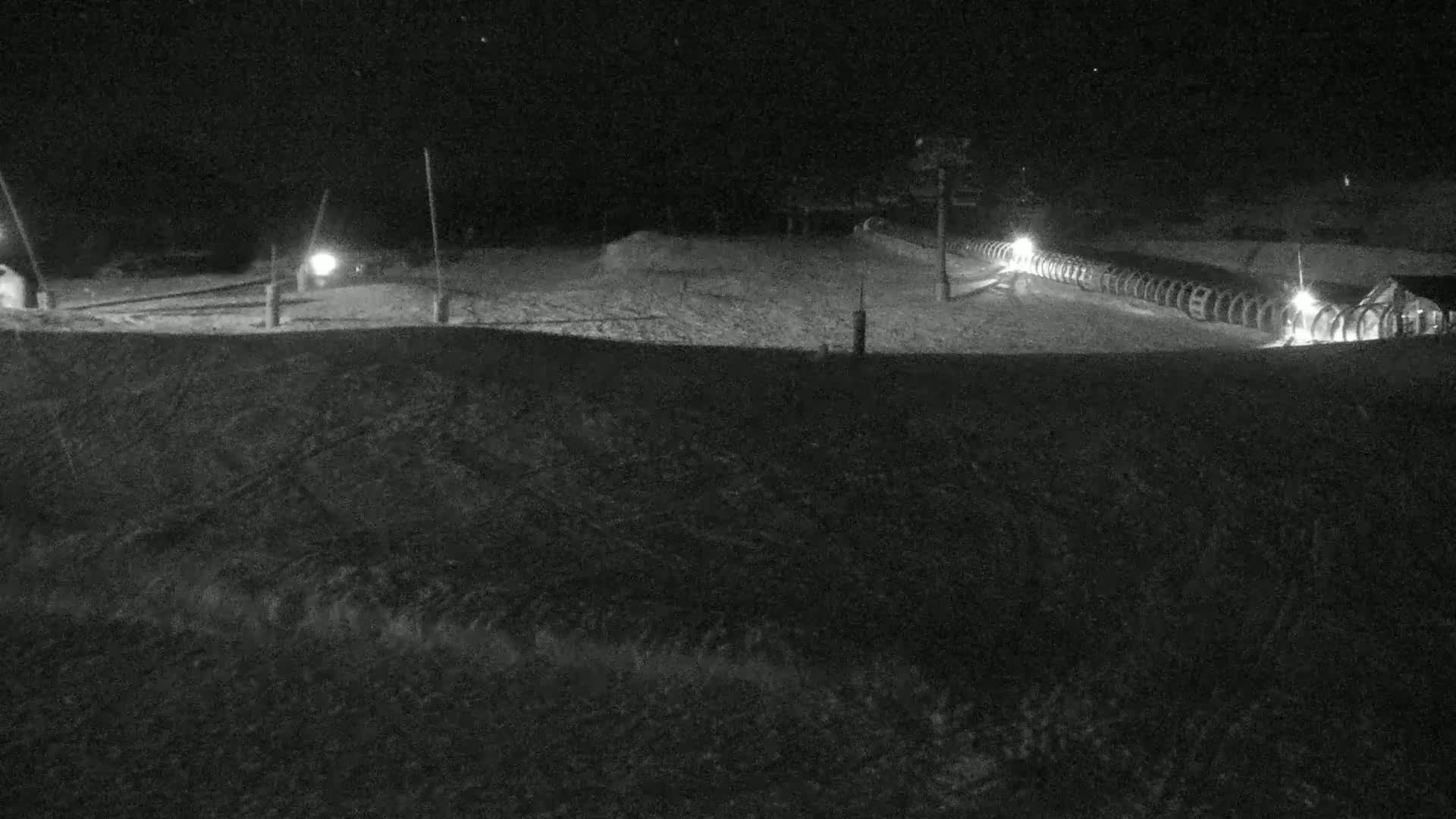 A snow-covered landscape at night, illuminated by several lights, shows a row of objects resembling spools or cylinders.