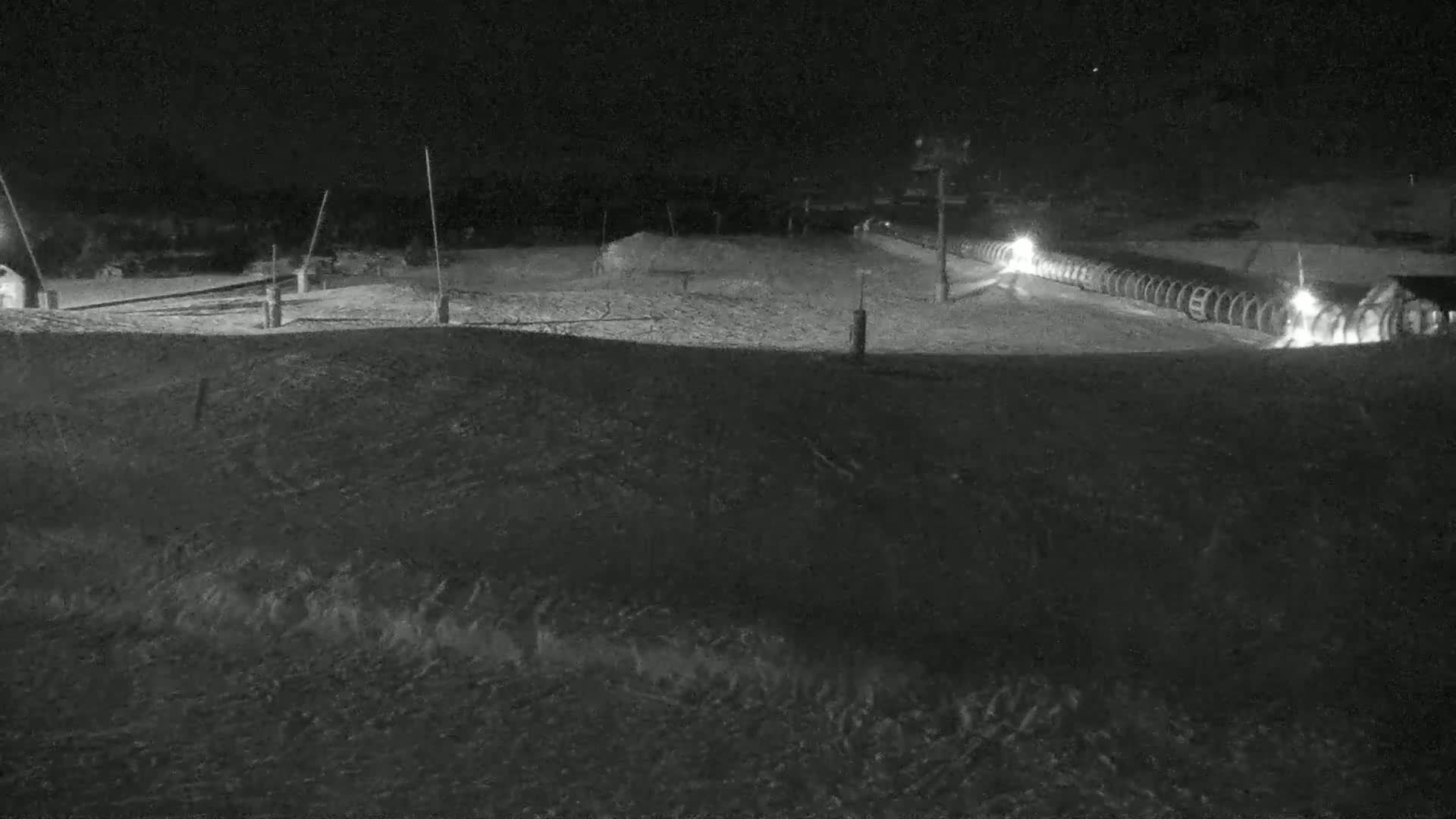 A snow-covered ski slope at night, illuminated by lights along a snowmaking system.