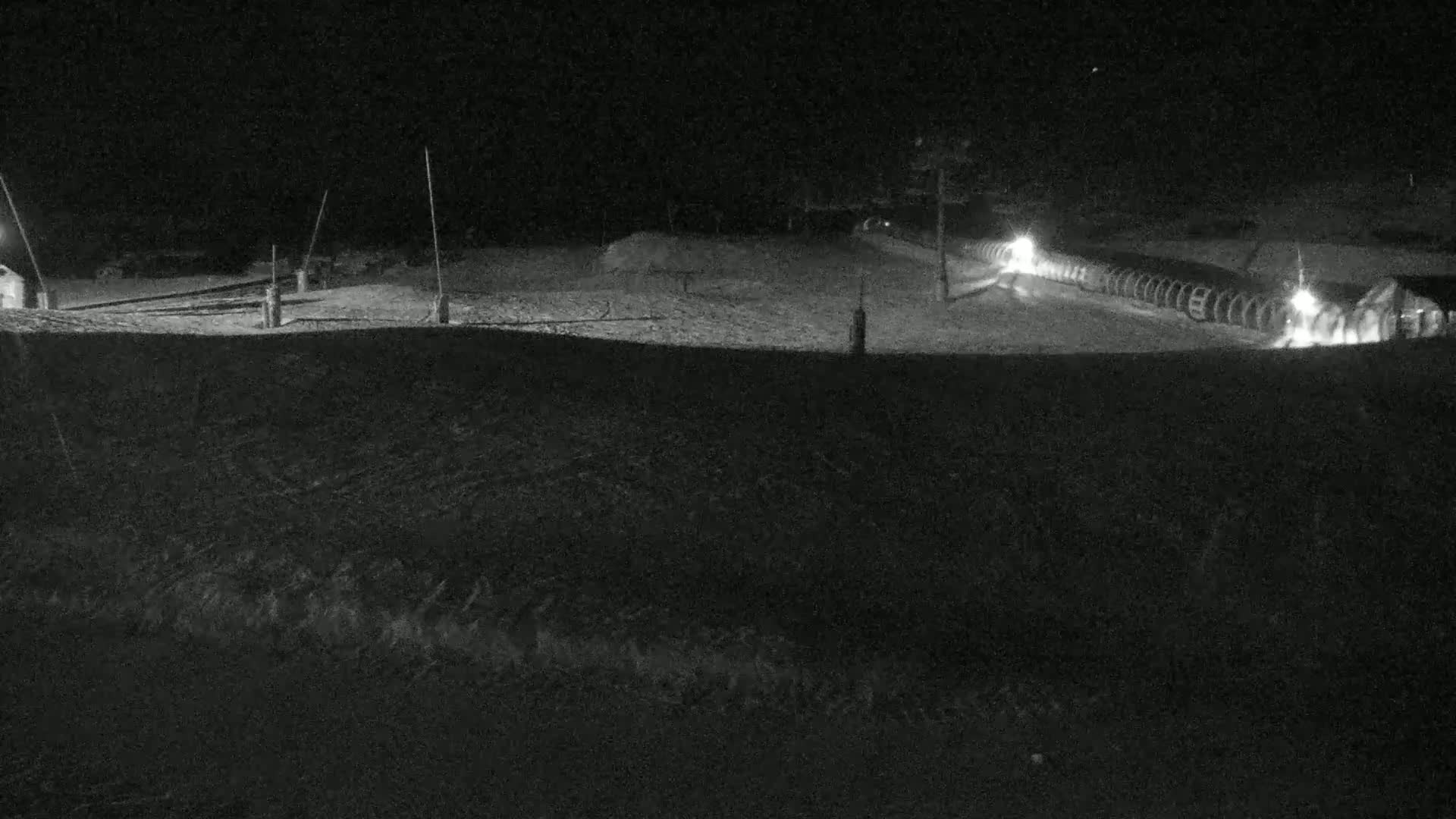 A nighttime, snow-covered landscape shows a lighted ski lift and a roadway with vehicles.