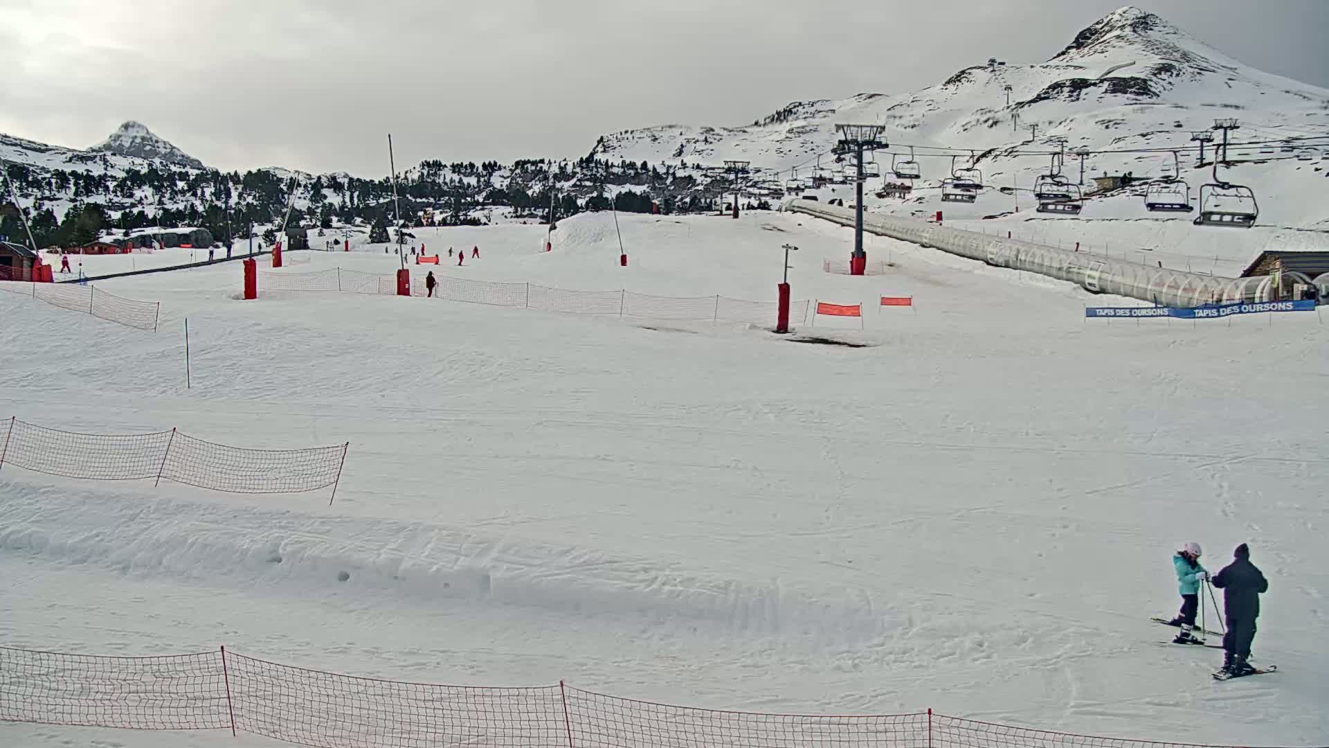 A snow-covered ski slope with several chairlifts and skiers, under an overcast sky.