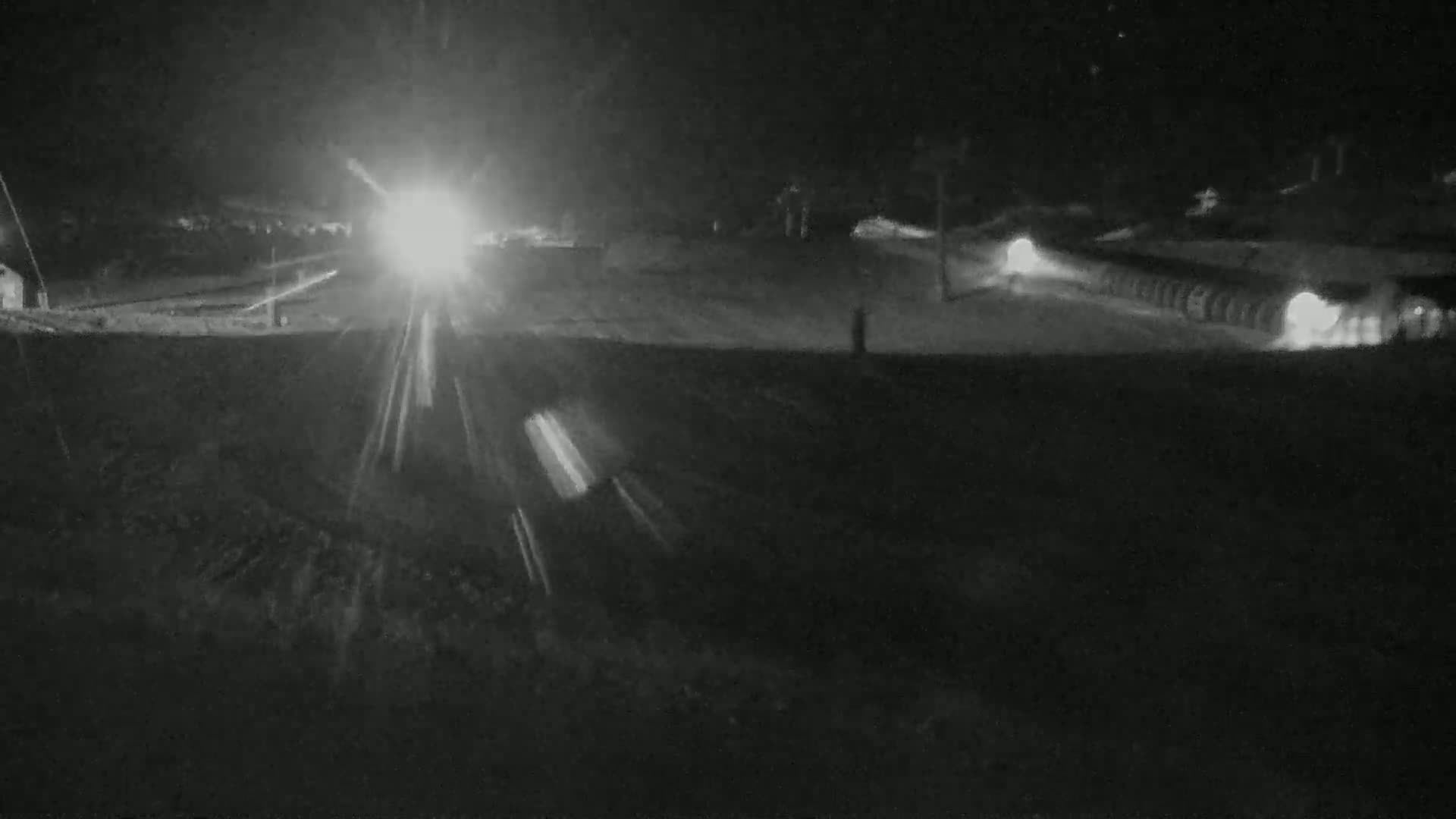 A nighttime, low-light view of a road with vehicles driving, appearing as bright streaks of light, and possibly snow or ice on the ground.