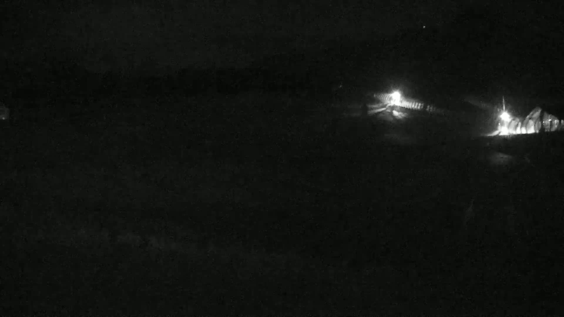 A dark, nighttime scene shows dimly lit structures in the distance.