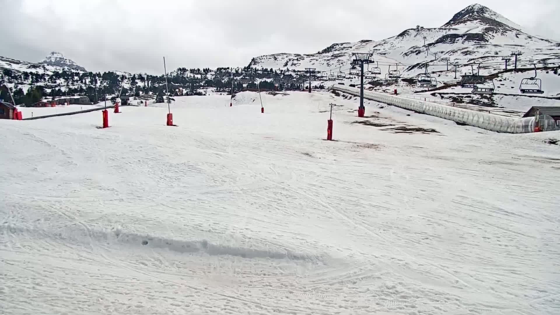 A snow-covered ski slope with a chairlift and several red markers is visible under an overcast sky.