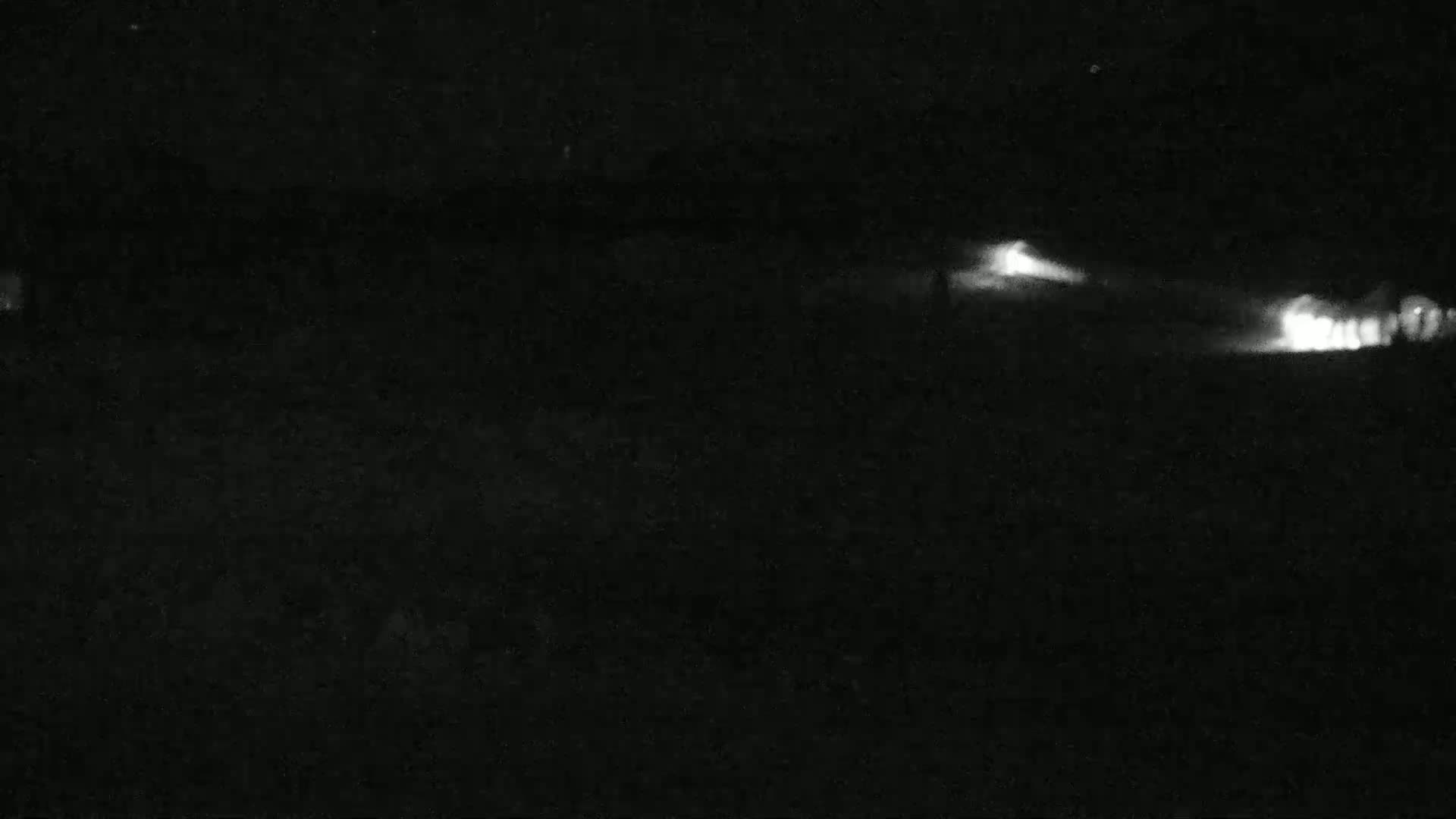 Headlights from vehicles are visible in the distance on a dark, nighttime road.