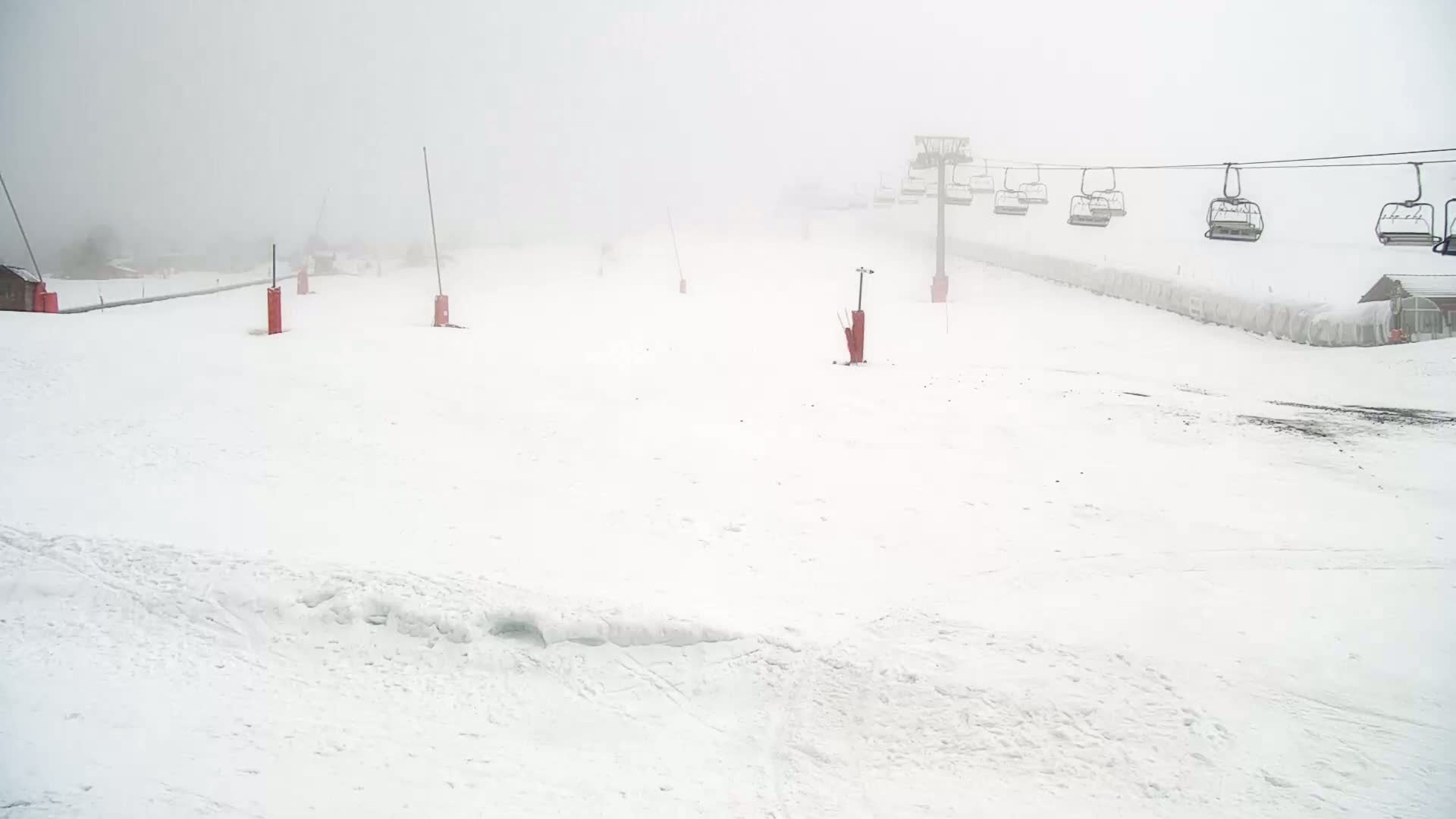 A snow-covered ski slope is visible in foggy conditions, with an empty chairlift overhead.
