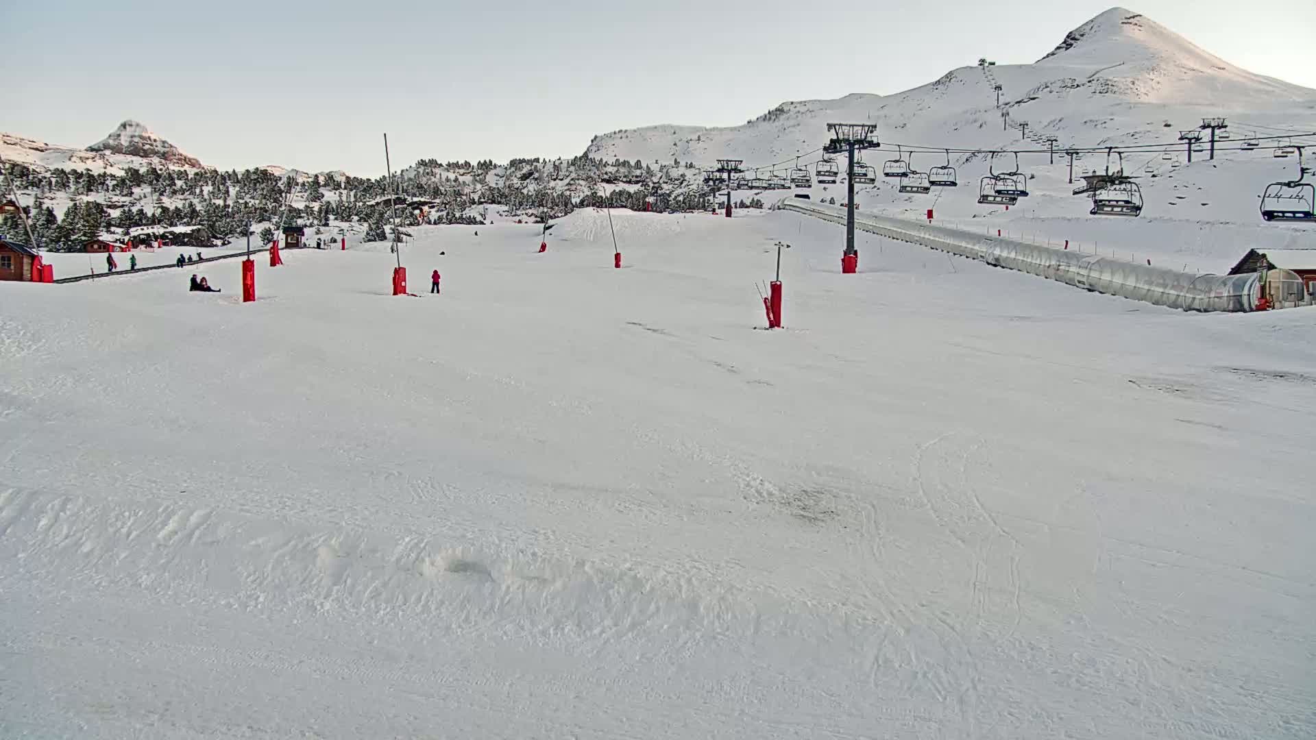 A snow-covered ski slope with a chairlift and several skiers visible under a clear sky.