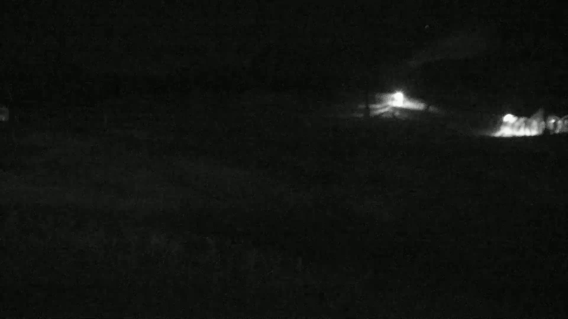 A nighttime, low-light image shows a dark, flat landscape with two distant, faint light sources.