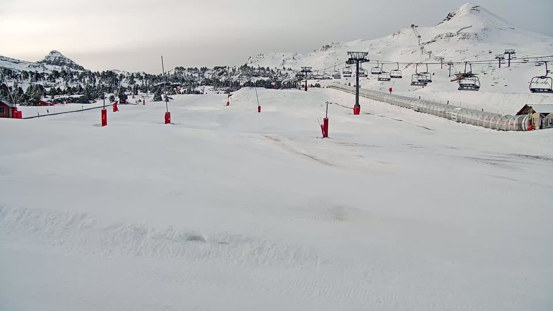 A snow-covered ski slope with a chairlift and several red markers under an overcast sky.