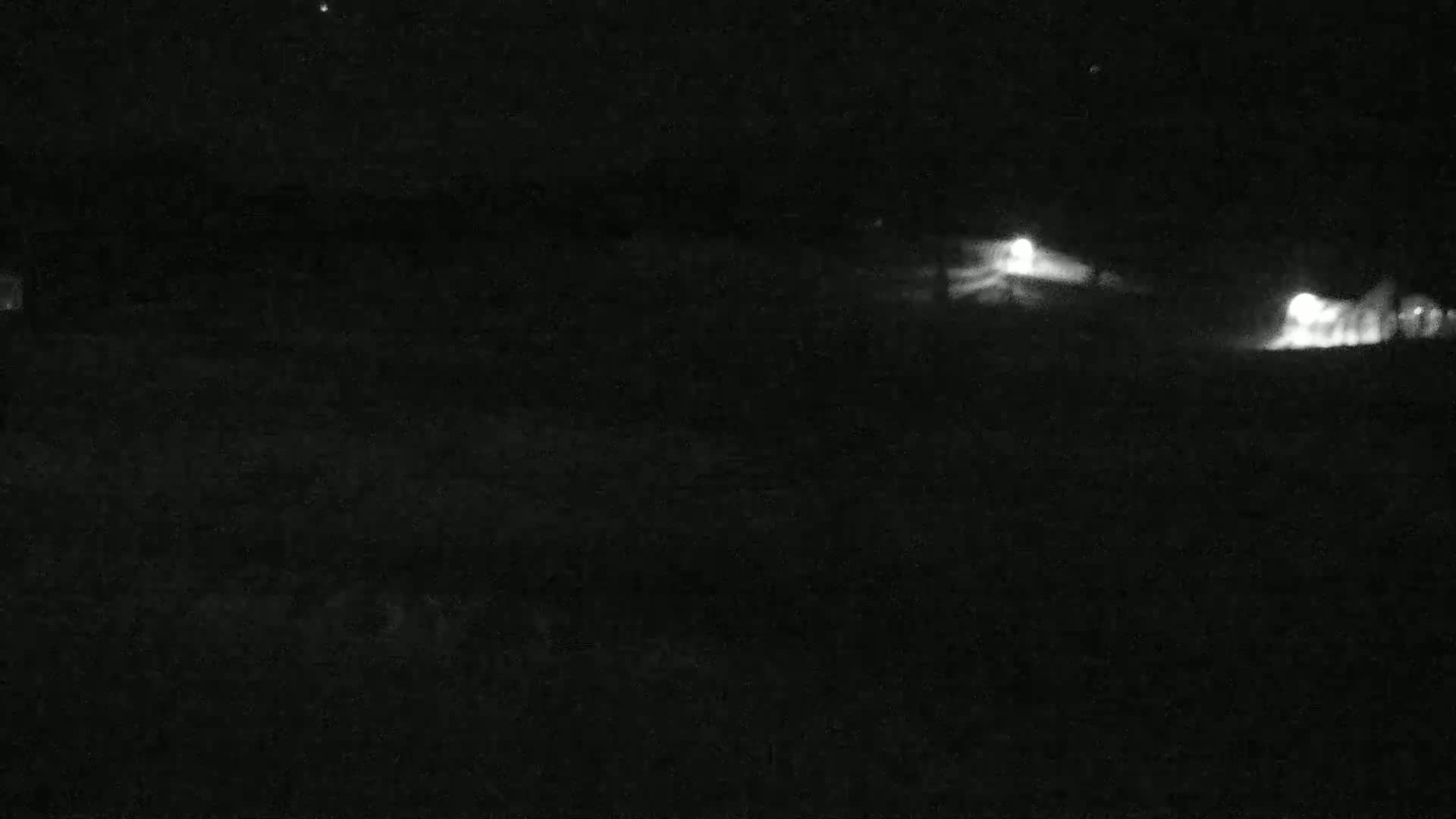 At night, two distant sources of light are visible in the dark, possibly headlights of vehicles on a road.