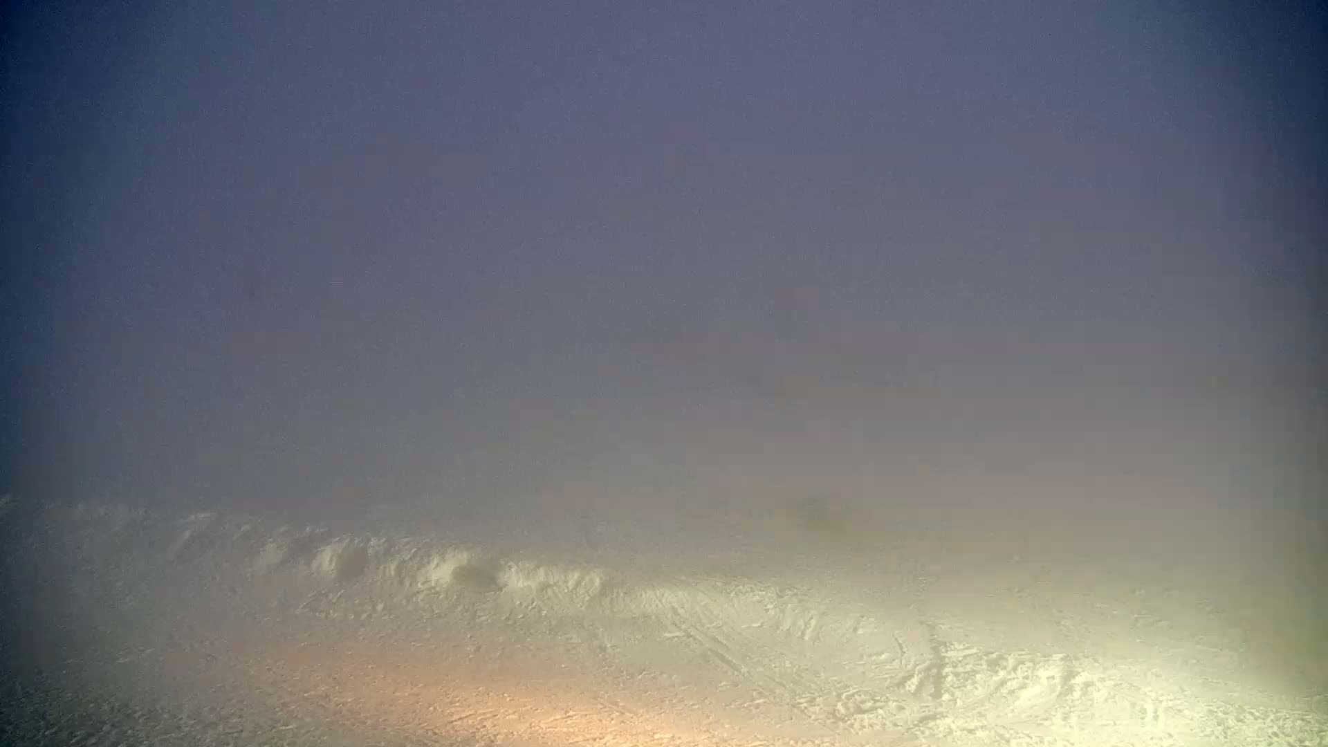 A snowy landscape is shrouded in a thick fog under a dusky purple sky.