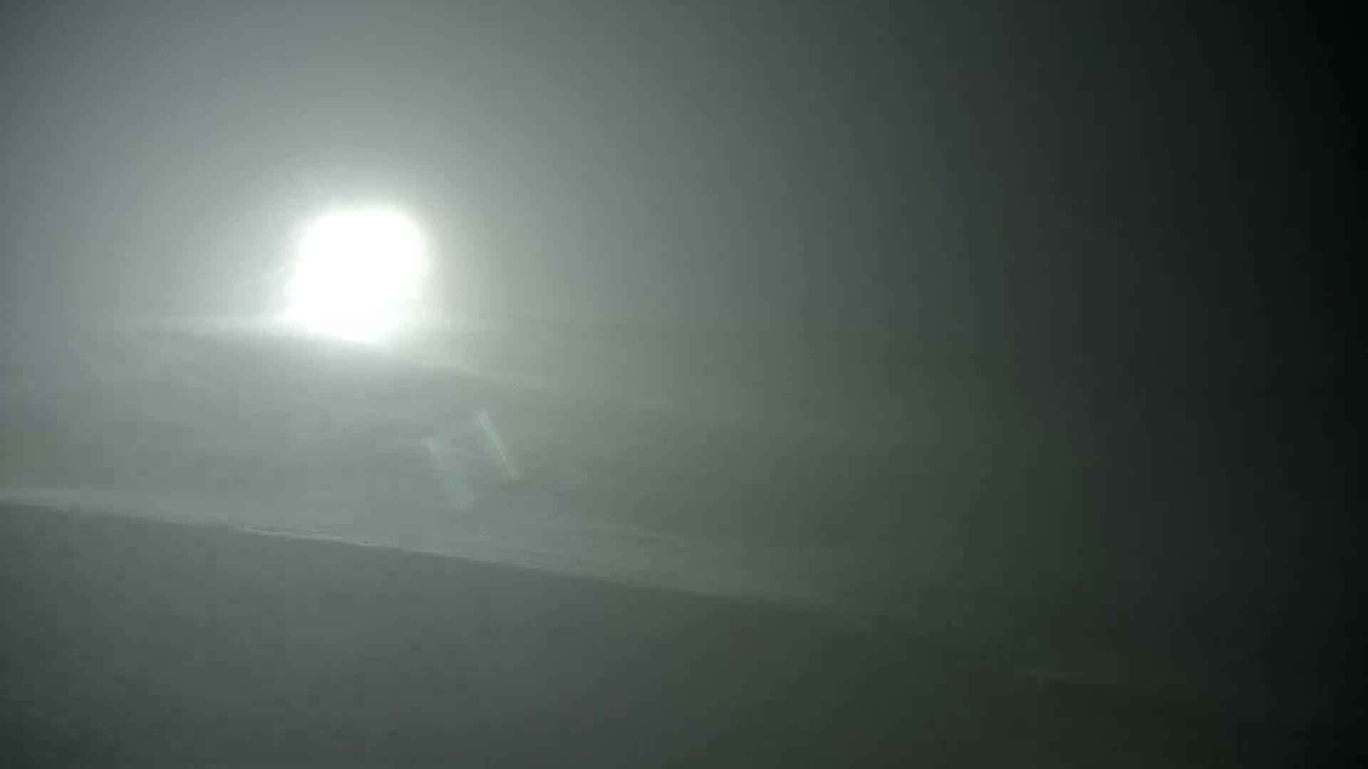 A bright sun is visible through a heavy fog obscuring a dark landscape.
